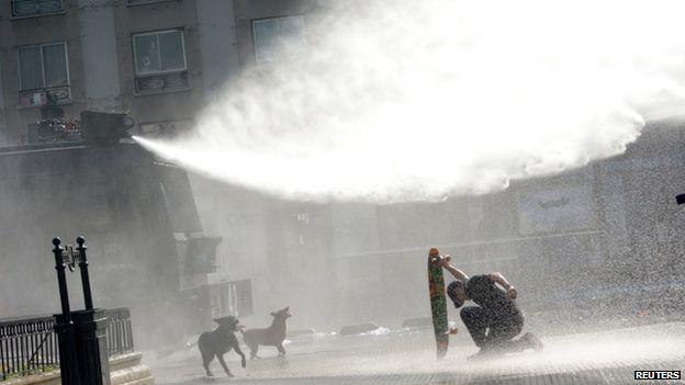 A protester kneels with his skateboard amidst water jets during a demonstration to demand changes in the education system at Santiago