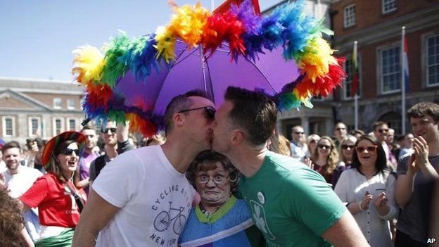 Two men kiss in front of cardboard cutout of popular Irish television character Mrs Brown