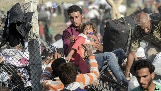 A man helps a girl over a fence on the Turkey-Syria border near Tal Abyad (14 June 2015)