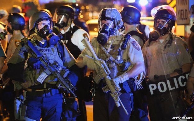 Police wearing gas masks and holding guns