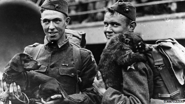 Two American soldiers about to embark for duty, with their pets, a dachshund and a racoon.