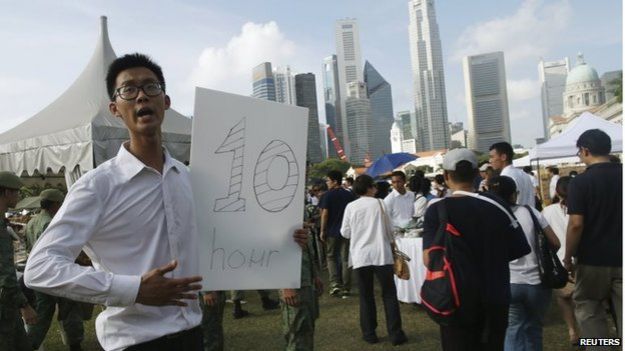 A man holds a sign with the estimated queue time in Singapore (27 March 2015)