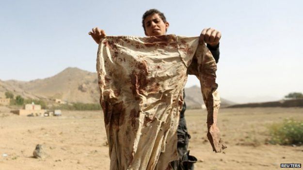A boy holds a blood-stained garment at the site of an air strike in the Yemeni village of Bait Rejal