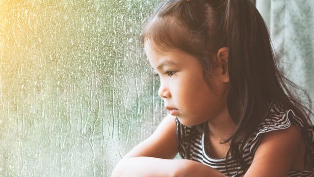 伤心的儿童女孩盯着下雨的窗外