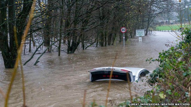 A near submerged car with its boot open, in a flooded road