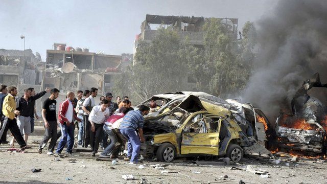 People and security personnel try to remove a car from an explosion site in Damascus
