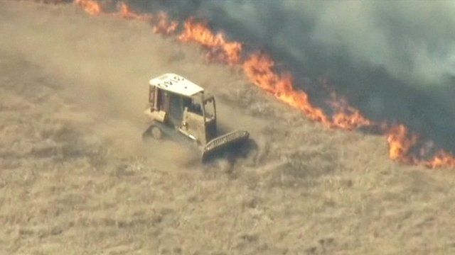A vehicle drives along a field next to a line of wildfire