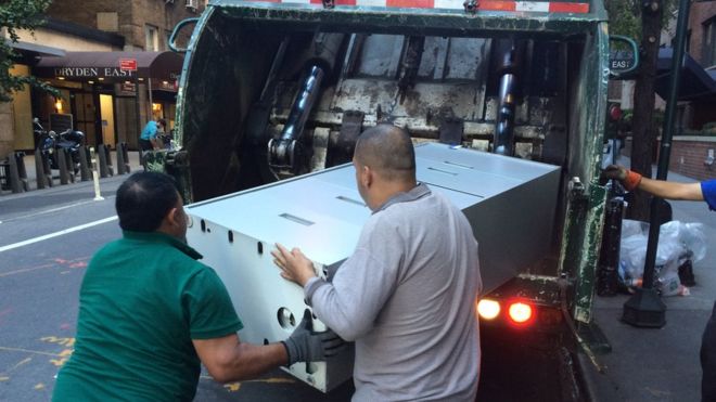 Dos hombres depositan un archivador en un camión de basura en Nueva York.