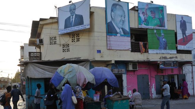 People walk past a house with billboards displaying portraits of incumbent Djibouti President Ismail Omar Guelleh in Djibouti