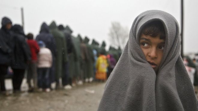 Migrant child covered in blanket stands in rain at Greek border camp near Idomeni, 10 March 2016