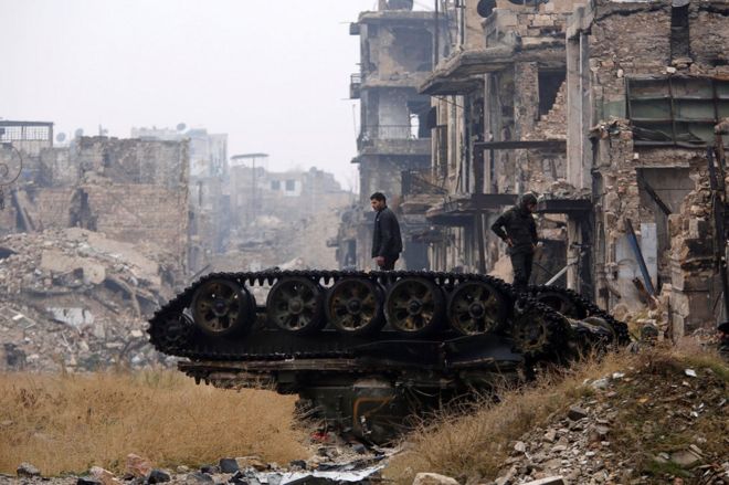 Forces loyal to Syria's President Bashar al-Assad stand atop a damaged tank near Umayyad mosque, in Aleppo, 13 December