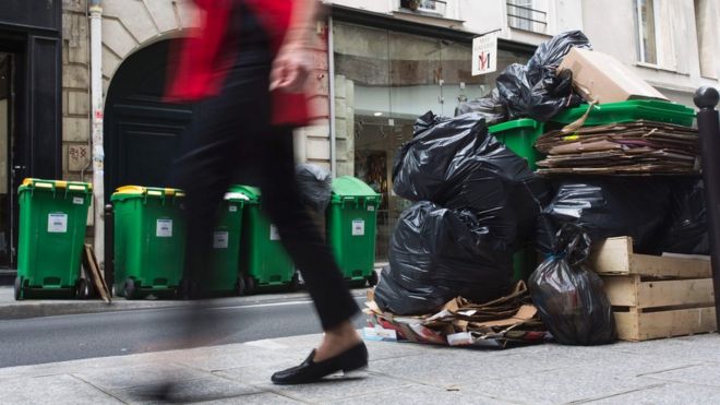 A woman walks past rubbish bins on June 8, 2016 in a street in Paris