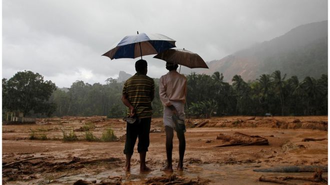 Two Sri Lankan landslide survivors stand on mud, holding their sandals and umbrellas, looking at a large area of mud after a landslide in Elangipitiya village in Aranayaka. Photo taken on 18 May 2016.