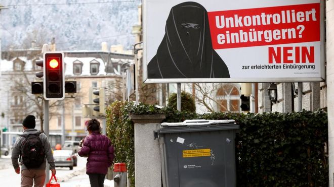 People walk past a poster of "Committee against an easier path to citizenship" on a display at the Hauptbahnhof central railway station in Zurich, 11 January 2017