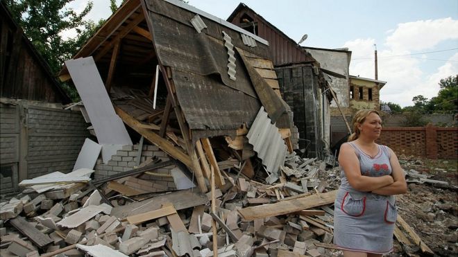 Женищна стоит рядом со своим разрушенным домом в Донецкой области