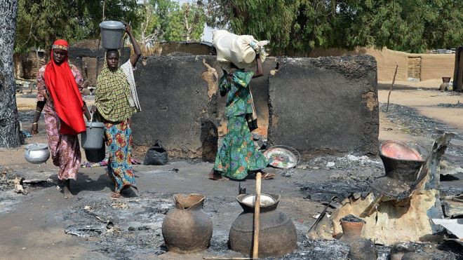Young girls fleeing from Boko Haram Islamists walk past burnt house and carries belongings at Mairi village outskirts of Maiduguri capital of north-east Borno state, on 6 February 2016