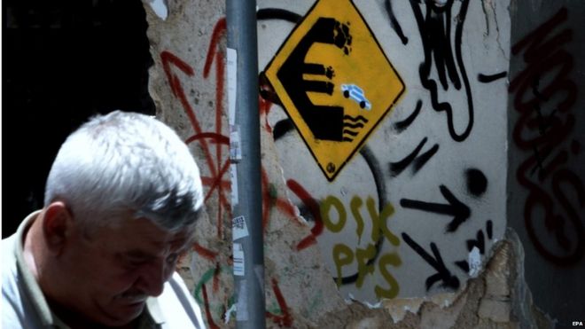 A man passes by a graffiti showing a euro sign and a car in the colours of Greece jumping off on the wall of an old house in Athens, Greece, on 24 June 2015