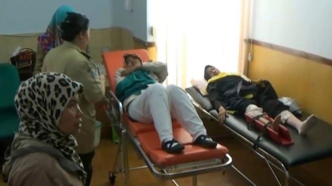 Two injured passengers lie on beds at a medical facility at Soekarno-Hatta International Airport, alongside three standing women, one of them in uniform