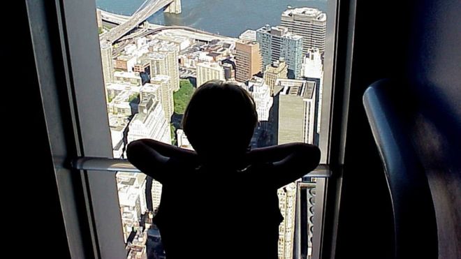 Criança olha cidade da janela de um apartamento