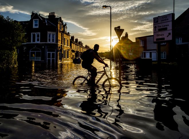 Велосипедист пересекает затопленную во время наводнения улицу