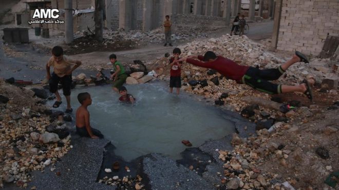 Photograph published by Aleppo Media Centre showing Syrian boys diving in a water-filled crater in the Sheikh Saeed district of Aleppo on 31 August 2016