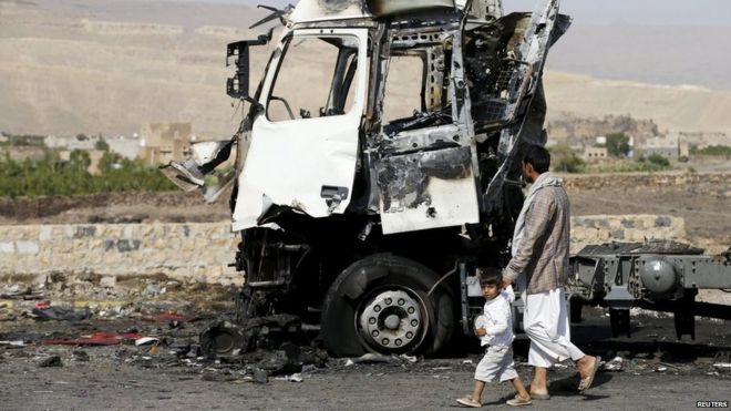 A man and his son walk past a truck hit by a Saudi-led air strike in Yemen"s northwestern province of Amran