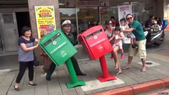 A postman and a family posing with the post boxes