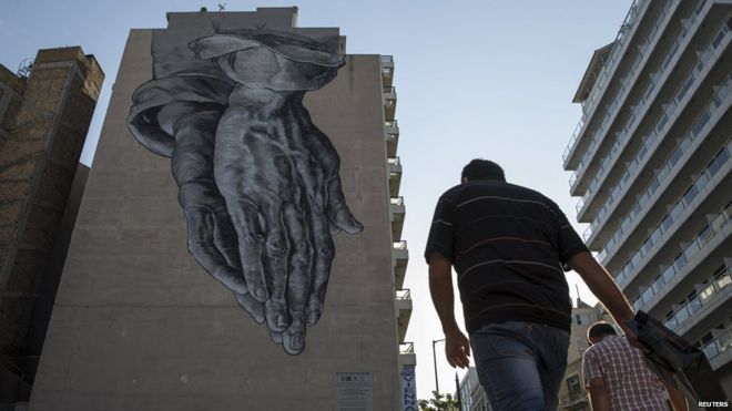 Man in Athens passes mural of praying hands