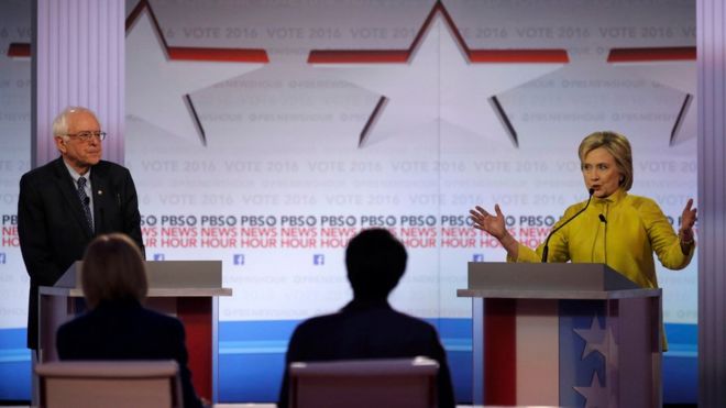 Democratic U.S. presidential candidate former Secretary of State Hillary Clinton speaks as Senator Bernie Sanders listens at the PBS NewsHour Democratic presidential candidates debate