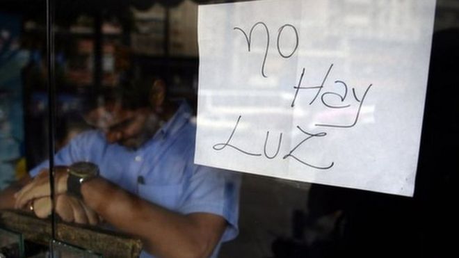 An employee of a business closed during a blackout stands behind the door with a notice reading "There's no electricity" in Caracas on 3 September, 2013