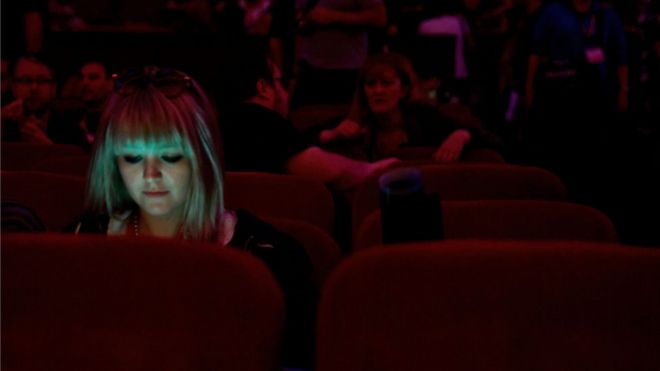 A young woman uses a phone in a cinema auditorium