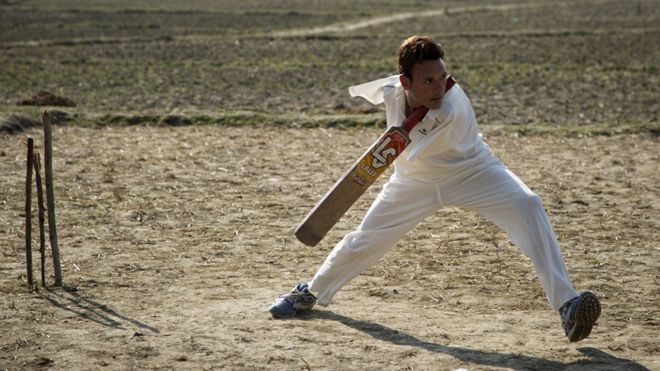 Amir holds the cricket bat between his neck and shoulder
