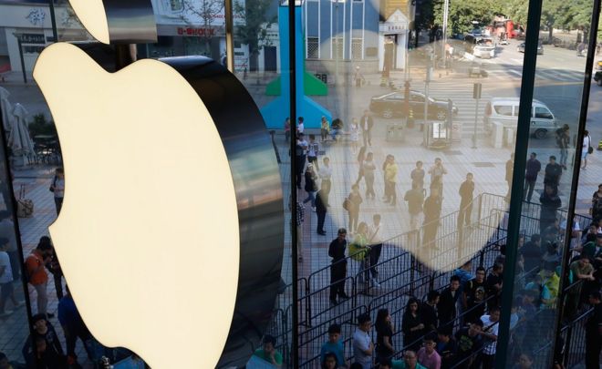 A window reflection of customers queue up outside an Apple store in Beijing