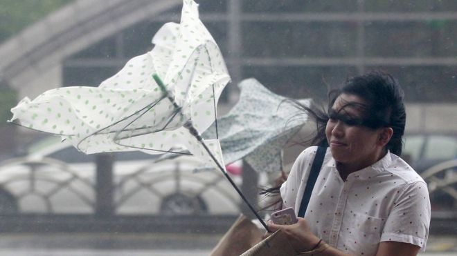 A woman holds onto her umbrella while walking against strong winds caused by Typhoon Dujuan in Taipei