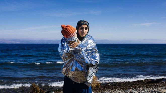 A woman holds her child wrapped in an emergency blanket shortly after arriving with other migrants and refugees on the Greek island of Lesbos