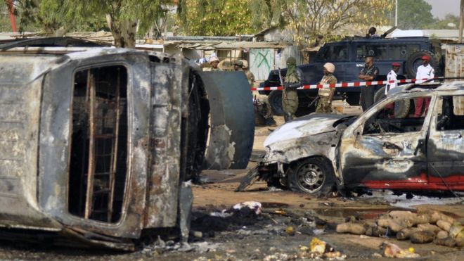 In this Tuesday Feb. 24, 2015 file photo, police officers stand guard following a suicide bomb explosion at a bus station in Kano, Nigeria