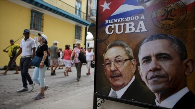 Tourists pass by images of U.S. President Barack Obama and Cuban President Raul Castro