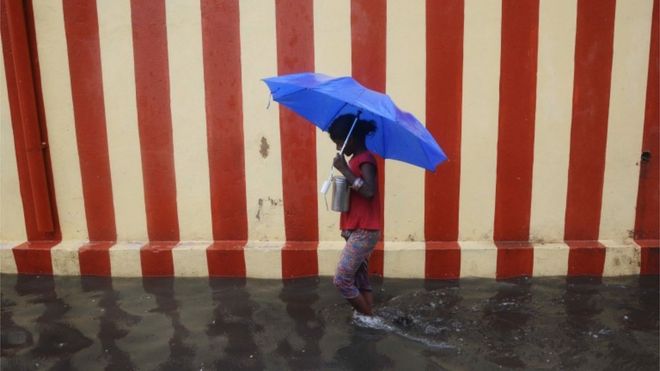An Indian girl walks under an umbrella along a waterlogged street following heavy rain in Chennai on November 13, 2015.