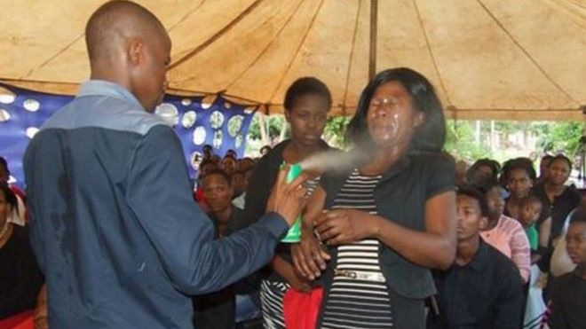 A man spraying insecticide in the face of a woman before a congragation.