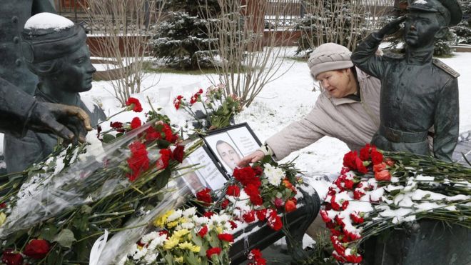 A woman lays flowers at a tribute to Lieutenant Colonel Oleg Peshkov (L) and marine Alexander Pozynich (R) in Moscow