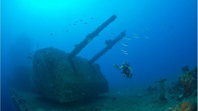 Buzo nada al lado de un buque de guerra hundido
