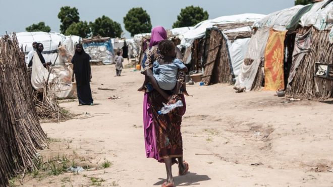 A woman carrying a child at her back walk through tents at the Muna makeshift camp for internally displaced people on the outskirts of Maiduguri, north-eastern Nigeria.