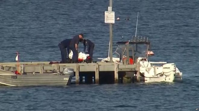 Police carry a body in a bag and place it in on a stretcher on a jetty in Triabunna, off the Australian island of Tasmania