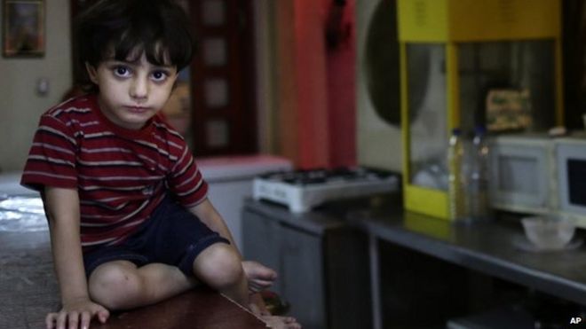 In this Sunday, 25 August, 2013 photo, a Syrian child watches as his mother who fled her home because of Syria's civil war prepares a meal in the kitchen at the Kertaj Hotel in Damascus, Syria.