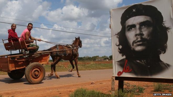 Two Cubans drive a horse and cart past a poster of Che Guevara