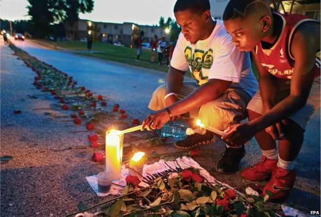 One of winning photographs taken by the staff of the St Louis Post-Dispatch shows a man and his brother lighting candles as roses stretch down the street near the spot where Michael Brown was shot in Ferguson