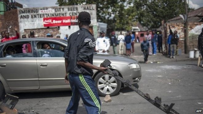 A man holds a piece of burnt wood as Zulu protesters demonstrate against foreign nationals in front of their hostel in the Jeppestown district of Johannesburg on 17 April 2015