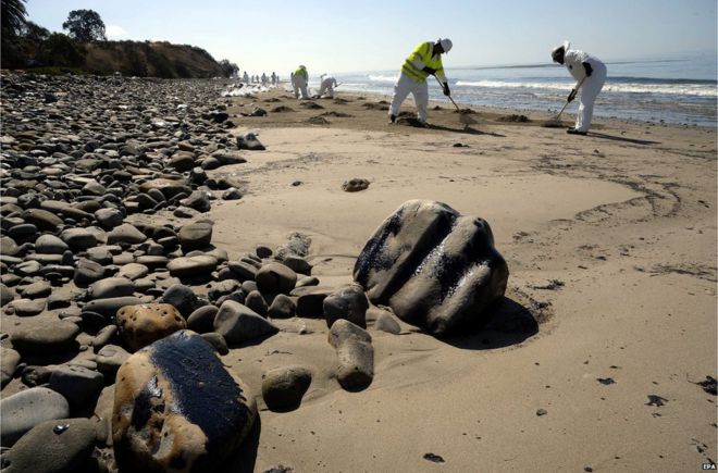 Workers cleaning the beach and rocks covered in oil