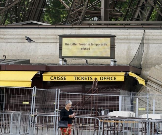A tourist uses her cell phone under the Eiffel Tower as an information board announces that the Eiffel Tower is temporarily closed, in Paris, 22 May 2015.