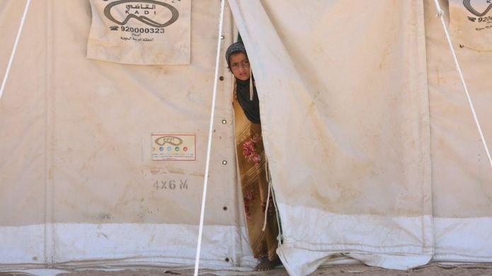 A girl stands in her family's tent at a camp for people displaced by conflict